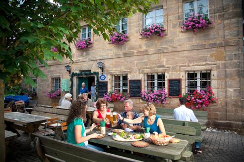 Bei der Brotzeit im Biergarten der Fuchsmühle bei Hilpoltstein stoßen Gäste mit kühlem Bier an und genießen die Köstlichkeiten.