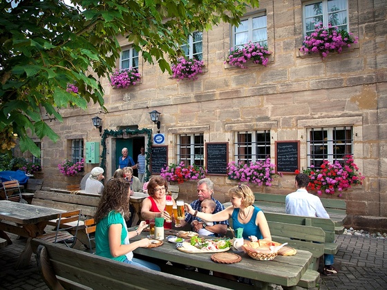 Bei der Brotzeit im Biergarten der Fuchsmühle bei Hilpoltstein stoßen Gäste mit kühlem Bier an und genießen die Köstlichkeiten.