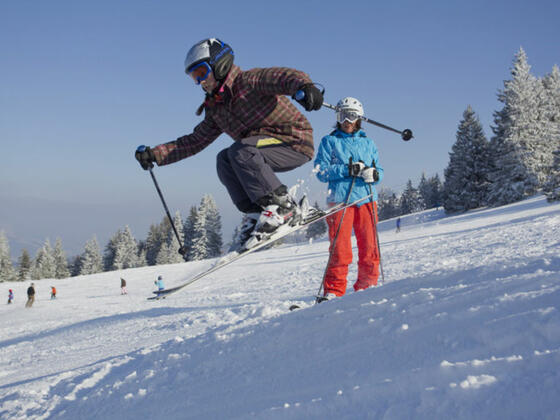 Mädchen in Skiausrüstung springt über eine Sprungschanze.
