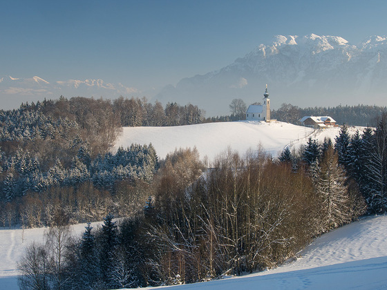 Kirche und Wirtshaus vor Bergkulissee: Johannishögl in Piding im Winter