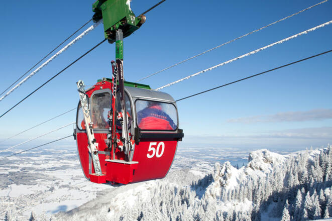 Rote Bergbahnkabine hoch über der Kampenwand. Blauer Himmel und weiße Bergspitzen.