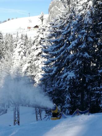 Schneekanone mit Haus im Hintergrund