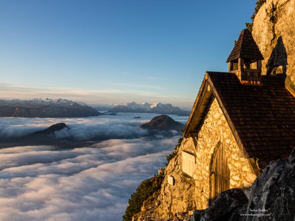 Das Tal noch unter dem Nebel, die Kapelle erstrahlt schon im Sonnenlicht.