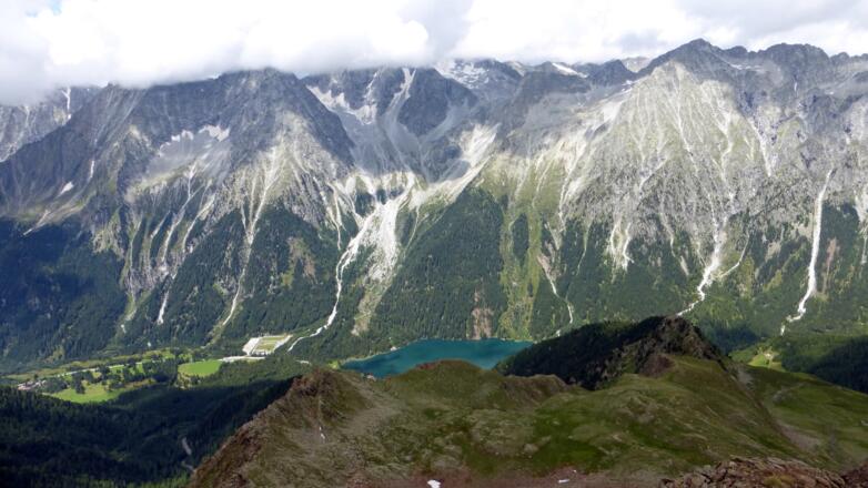 Hochgall und Wildgall sind wolkenverhangen; unten das Biathlonstadion und der Antholzer See