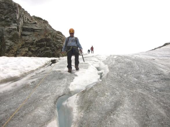 Knapp links (im Sinne des Abstiegs) des Felskopfs in der Flanke weiter nach unten (knapp 40°, steilstes Teilstück des Abstiegs). Die Instruktoren im Bild wählten hier als Sicherungsmethode ein Geländerseil (Fixseil).