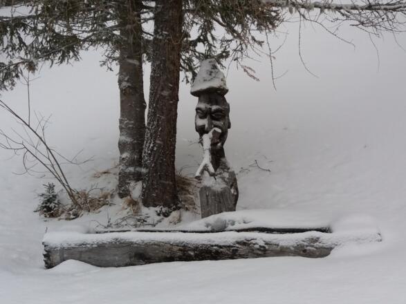 Geschnitzter Wasserzulauf am Brunnen vor der Heisshütte.