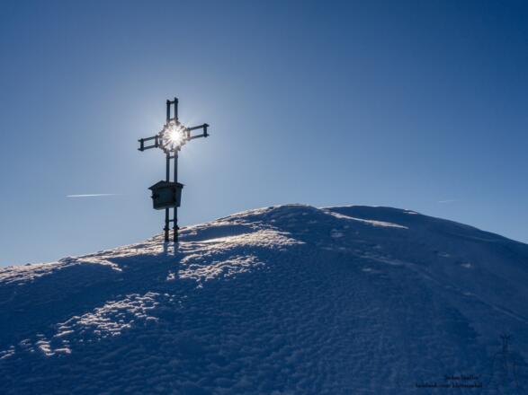 die Sonne strahlt durchs Gipfelkreuz