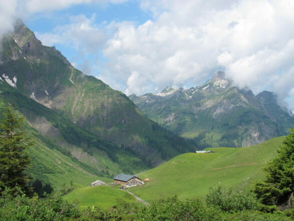Die Batzenalpe, in deren altem Gebäude sich das Alpmuseum uf m Tannberg befindet. Dahinter ist die Walser Heimat uf m Büel zu erkennen. Im Hintergrund die Hochkünzelspitze